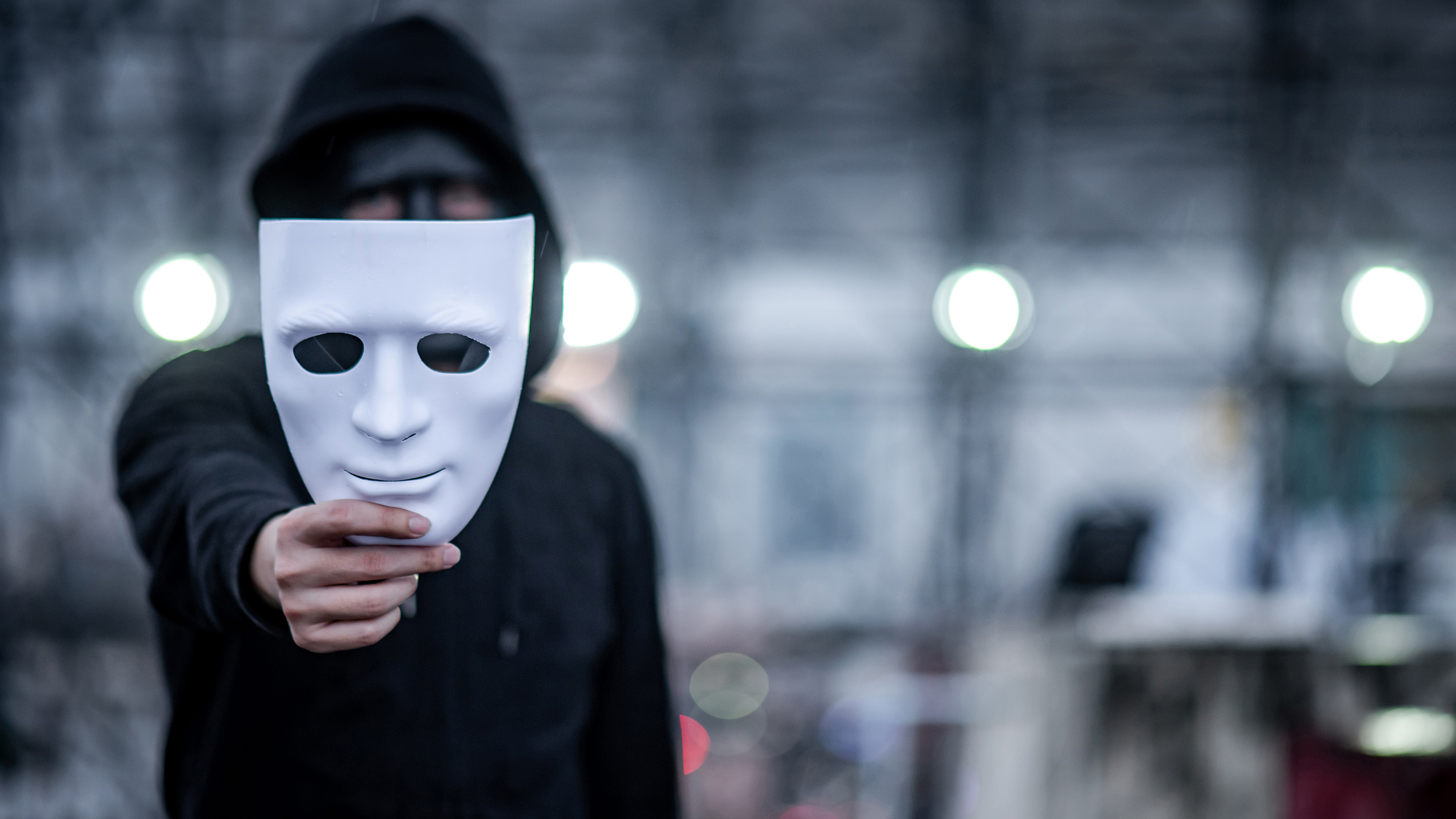 Mystery hoodie man with black mask holding white mask in his hand. Anonymous social masking or bipolar disorder concept.
