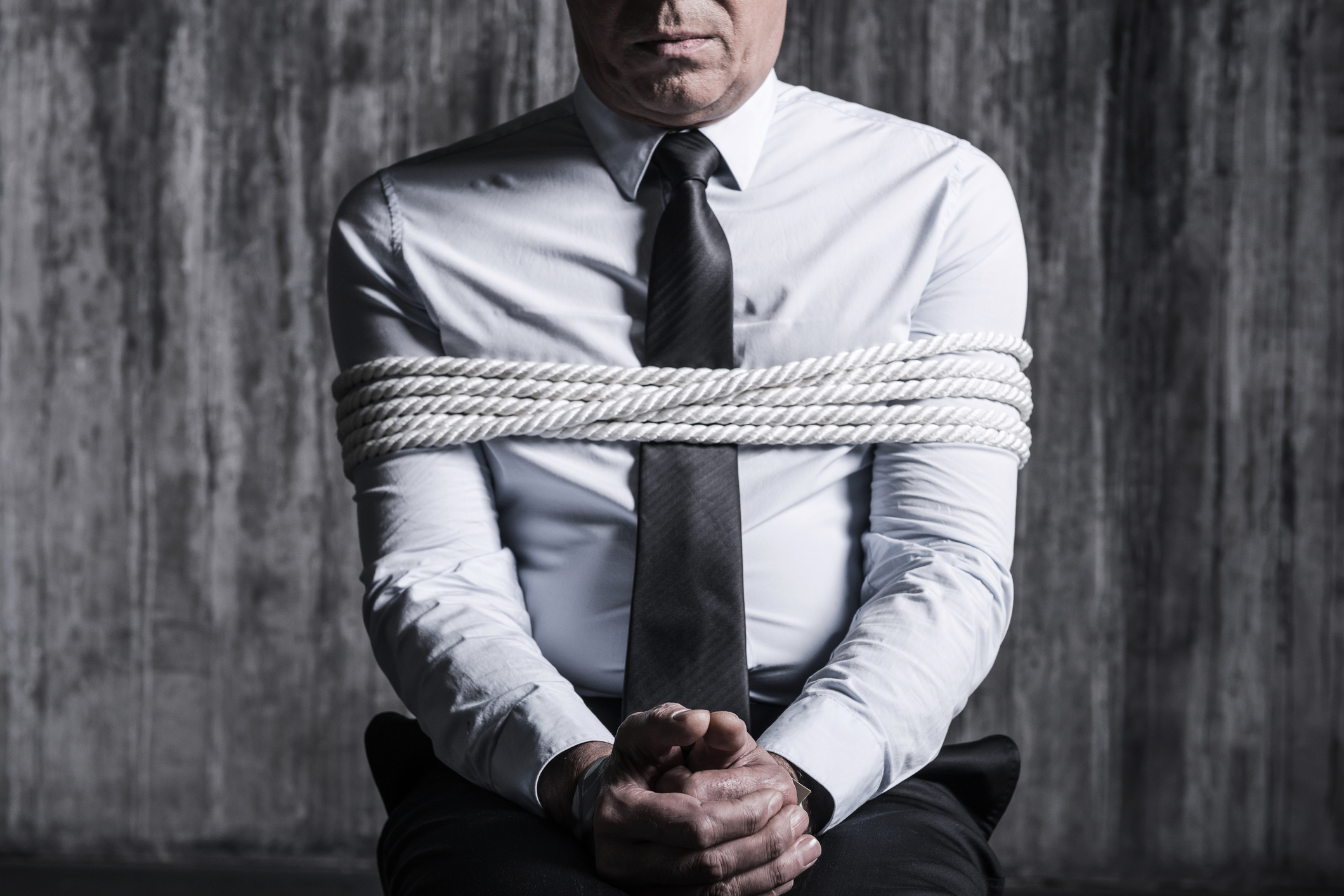 Cropped image of tied up businessman sitting at the chair with dirty wall  in the background